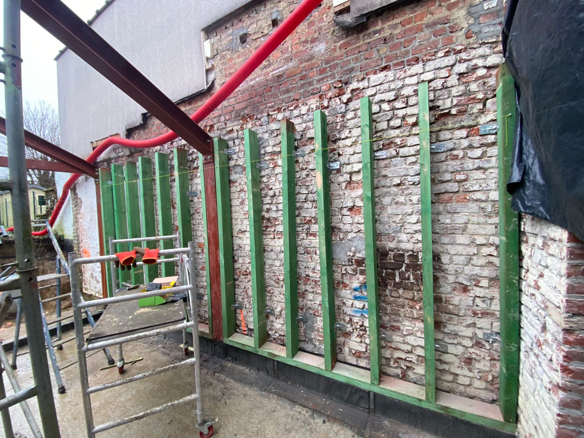 Ściana z cegły z drewnianą konstrukcją wzmacniającą i czerwonymi rurami, widok z rusztowania w Sępólnie Krajeńskim.