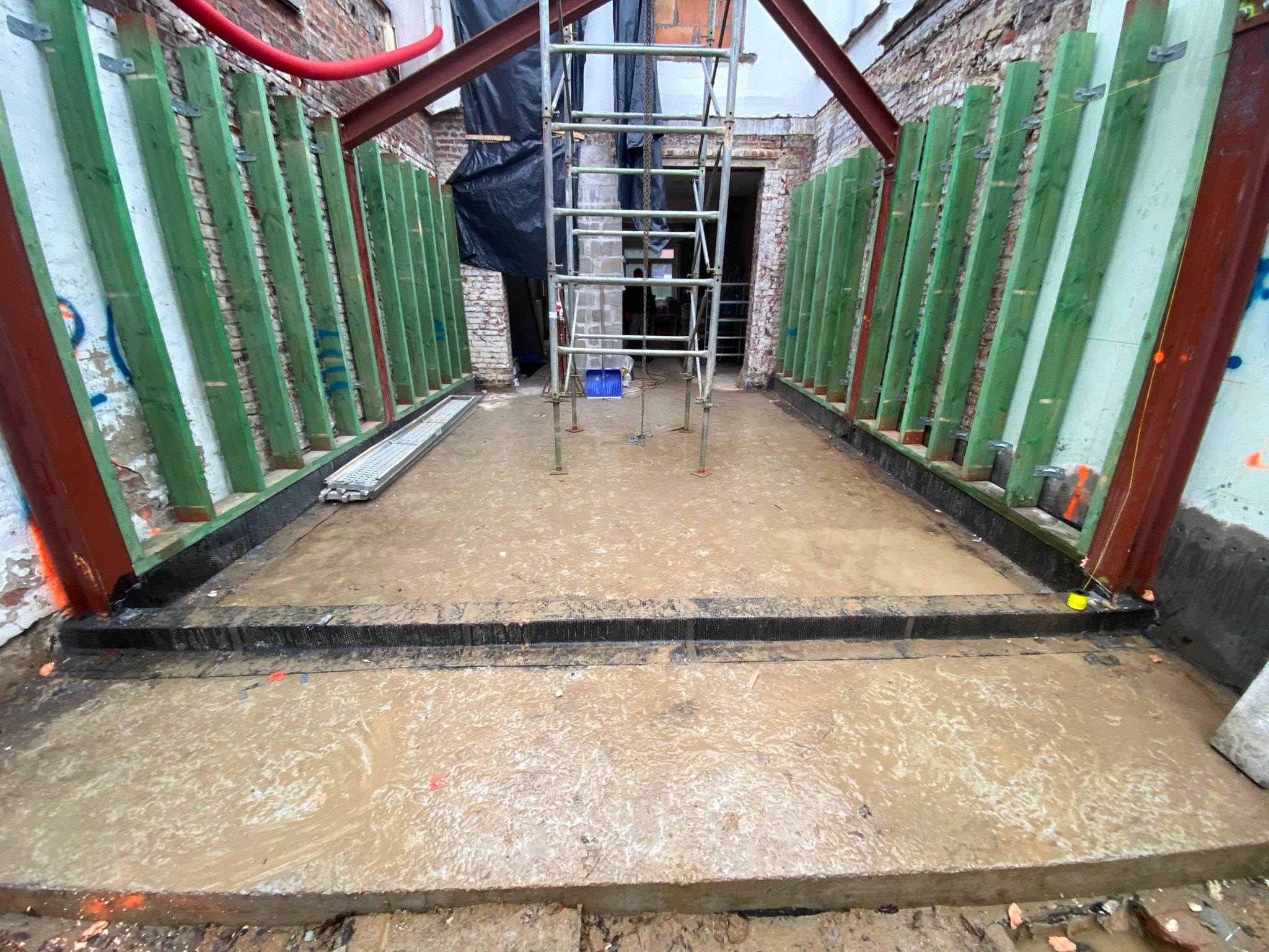 Przygotowany fundament pod budynek z deskowaniem, stalowymi belkami i rusztowaniem w tle, zalany wodą.