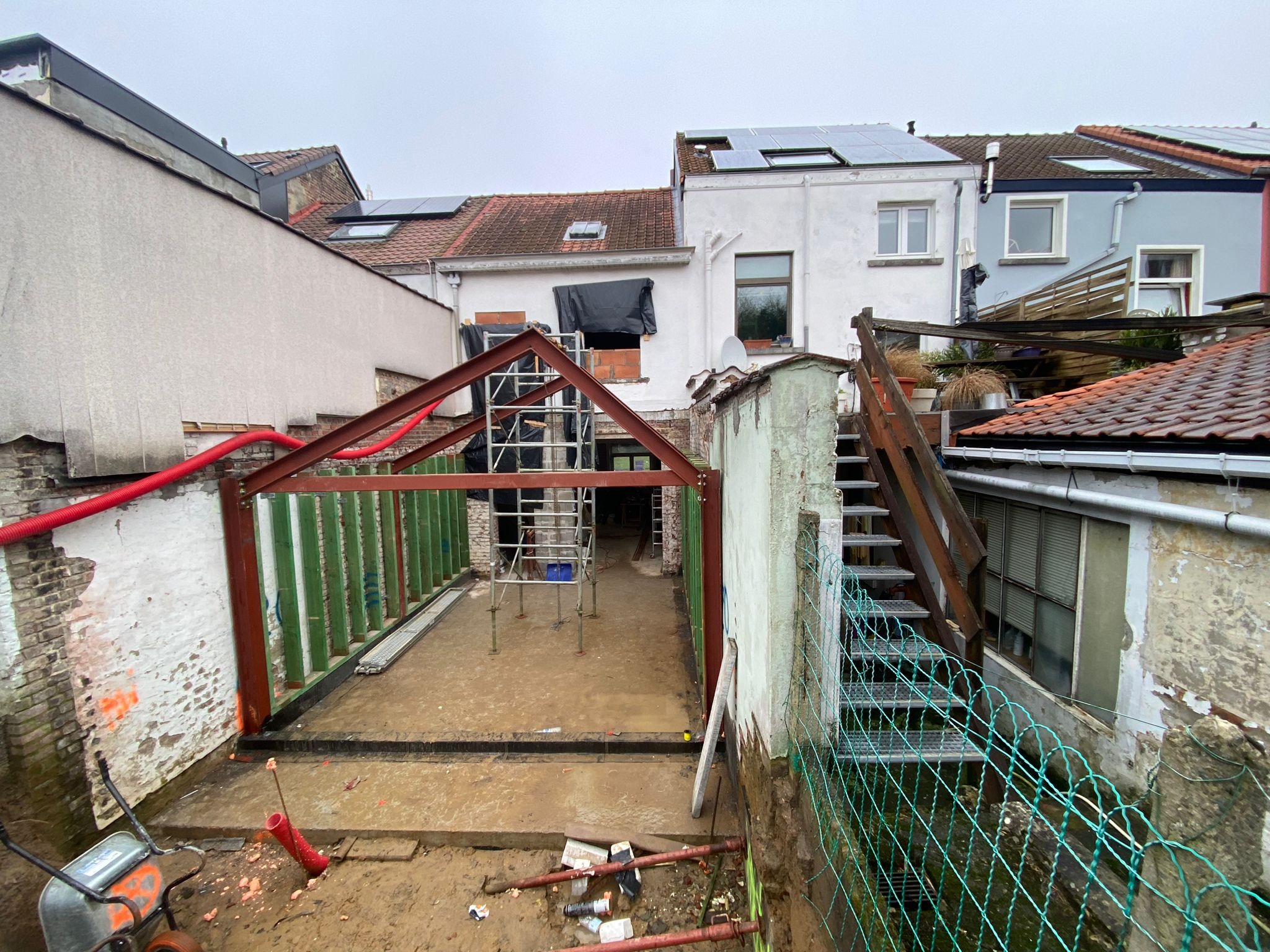 Budowa domu murowanego w trakcie realizacji: widok na konstrukcję stalową, rusztowania i przygotowany teren pod wylewkę, z widocznymi elementami instalacji i sąsiednią zabudową.