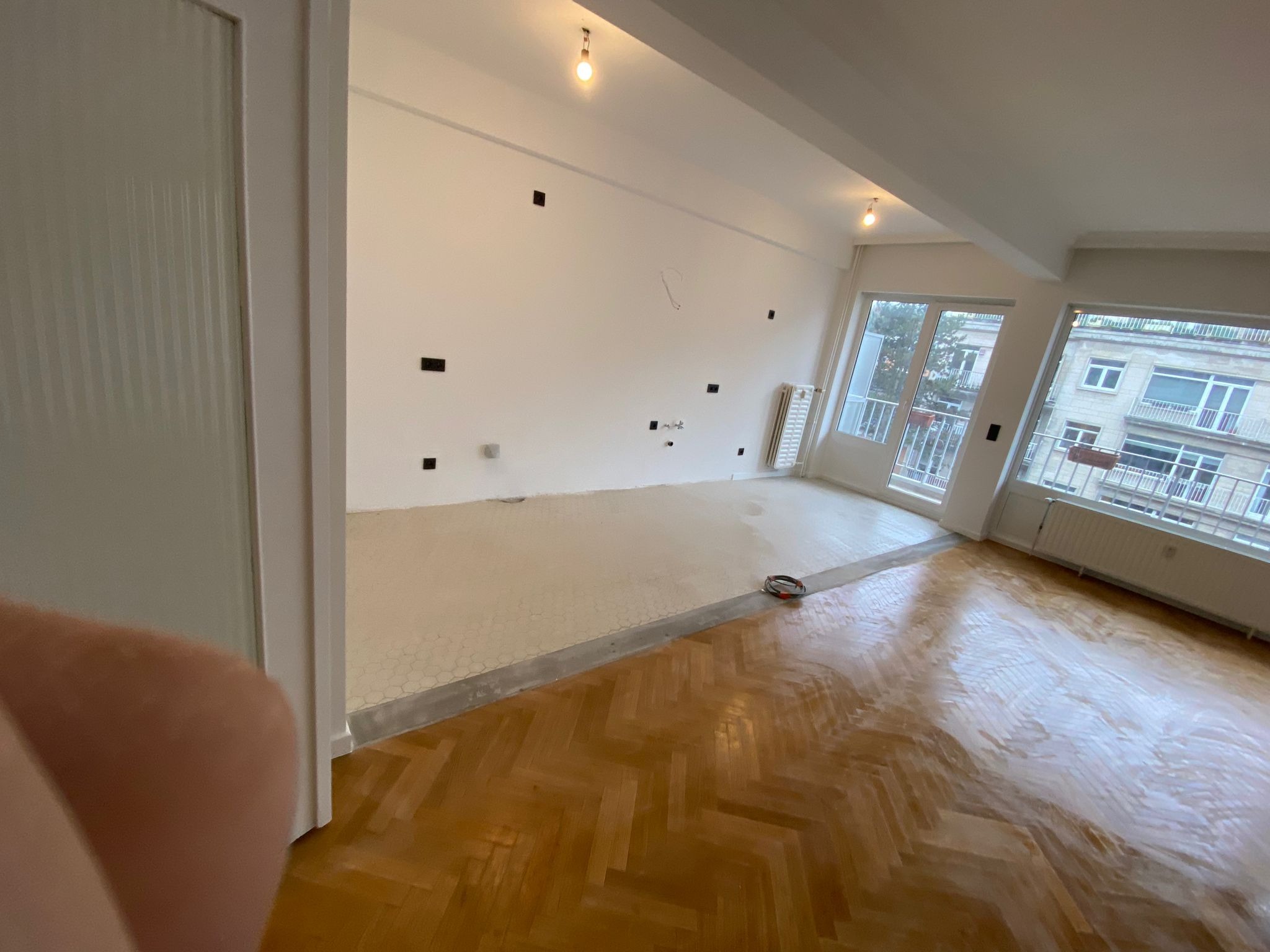 Pokój w trakcie remontu: parkiet po cyklinowaniu i fragment ściany przygotowany do malowania z widocznymi puszkami elektrycznymi.