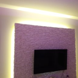 Adam Milczarek - Ściana z dekoracyjną okładziną kamienną, podświetlona pionowymi pasami LED po bokach, z zamontowanym telewizorem na środku.