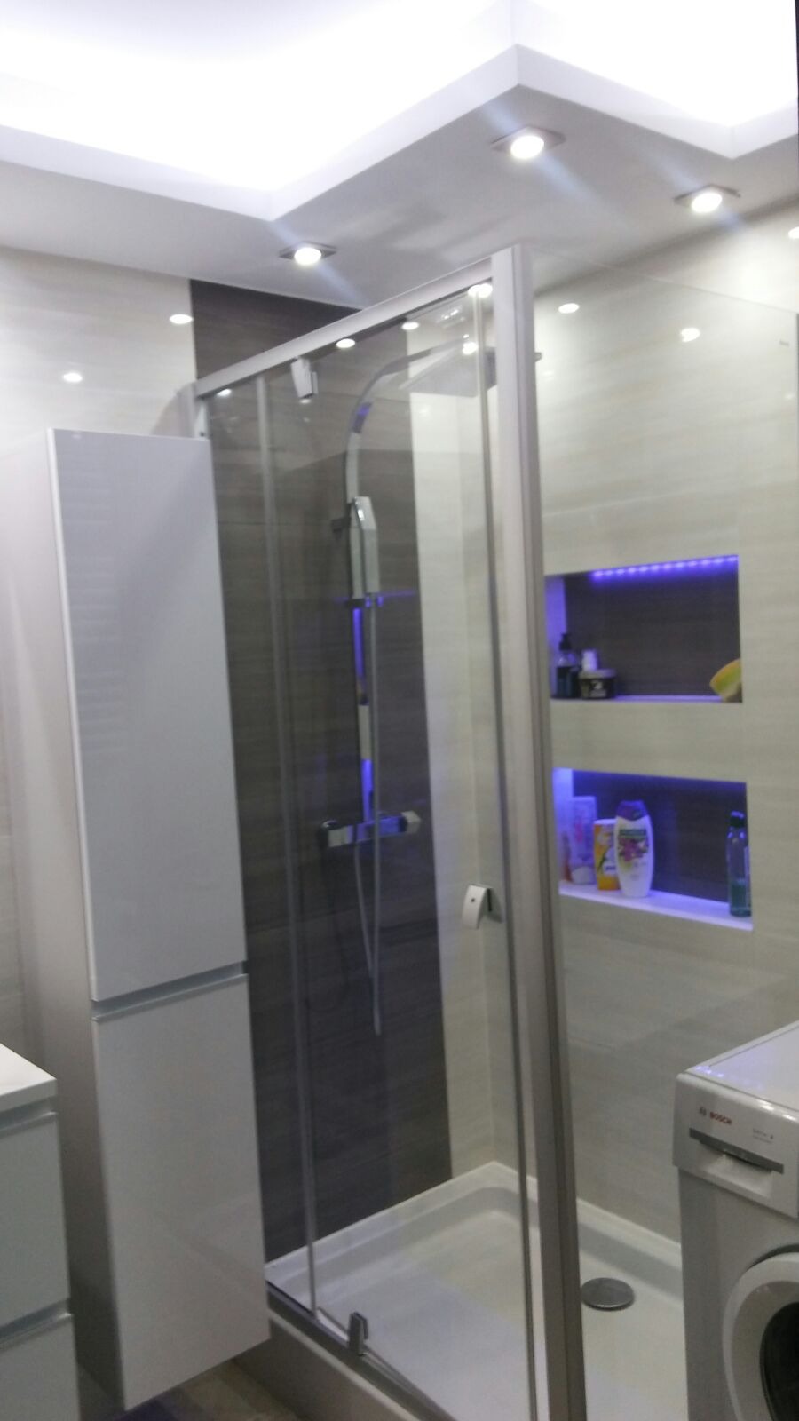 Nowoczesna łazienka z kabiną prysznicową typu walk-in, podświetlanymi niszami na kosmetyki i pralką Bosch.