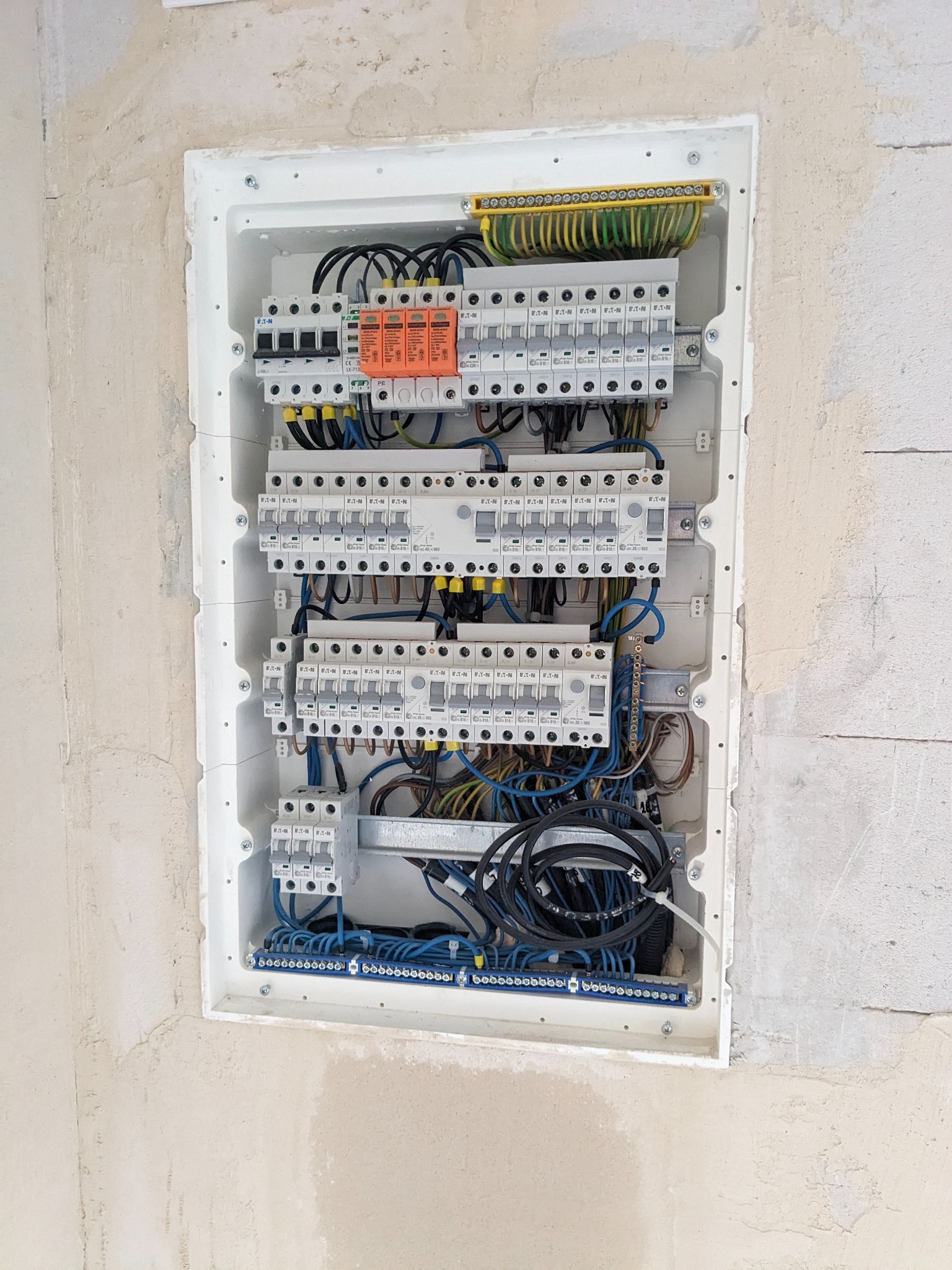 Rozdzielnica elektryczna z zabezpieczeniami przepięciowymi Eaton zamontowana na surowej ścianie w Helenowie Drugim, widoczne liczne przewody i złączki.