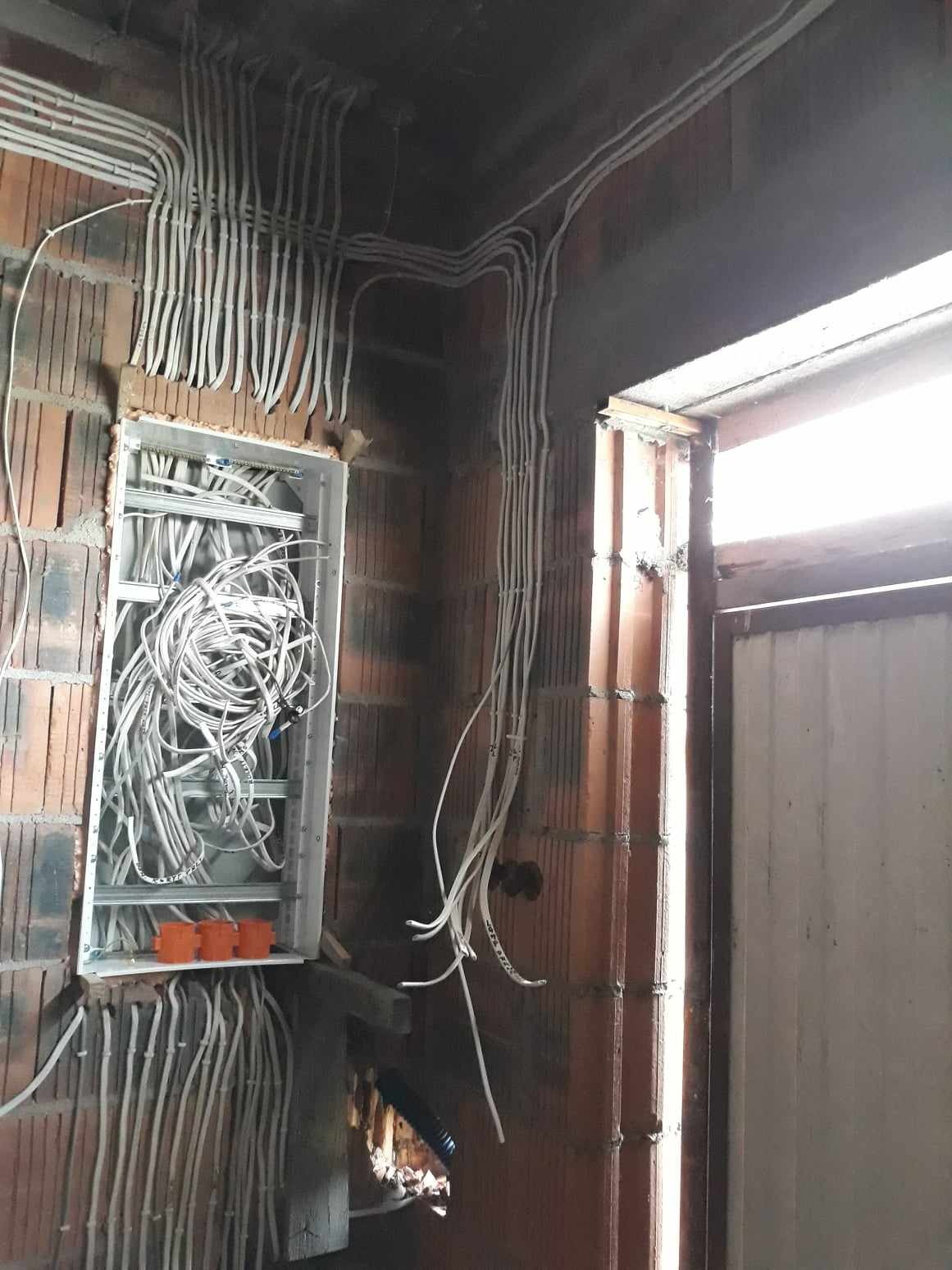 Wewnętrzne rozprowadzenie przewodów elektrycznych w budynku w trakcie budowy, widoczna puszka rozdzielcza z niepodłączonymi przewodami, ściany z cegły dziurawki.