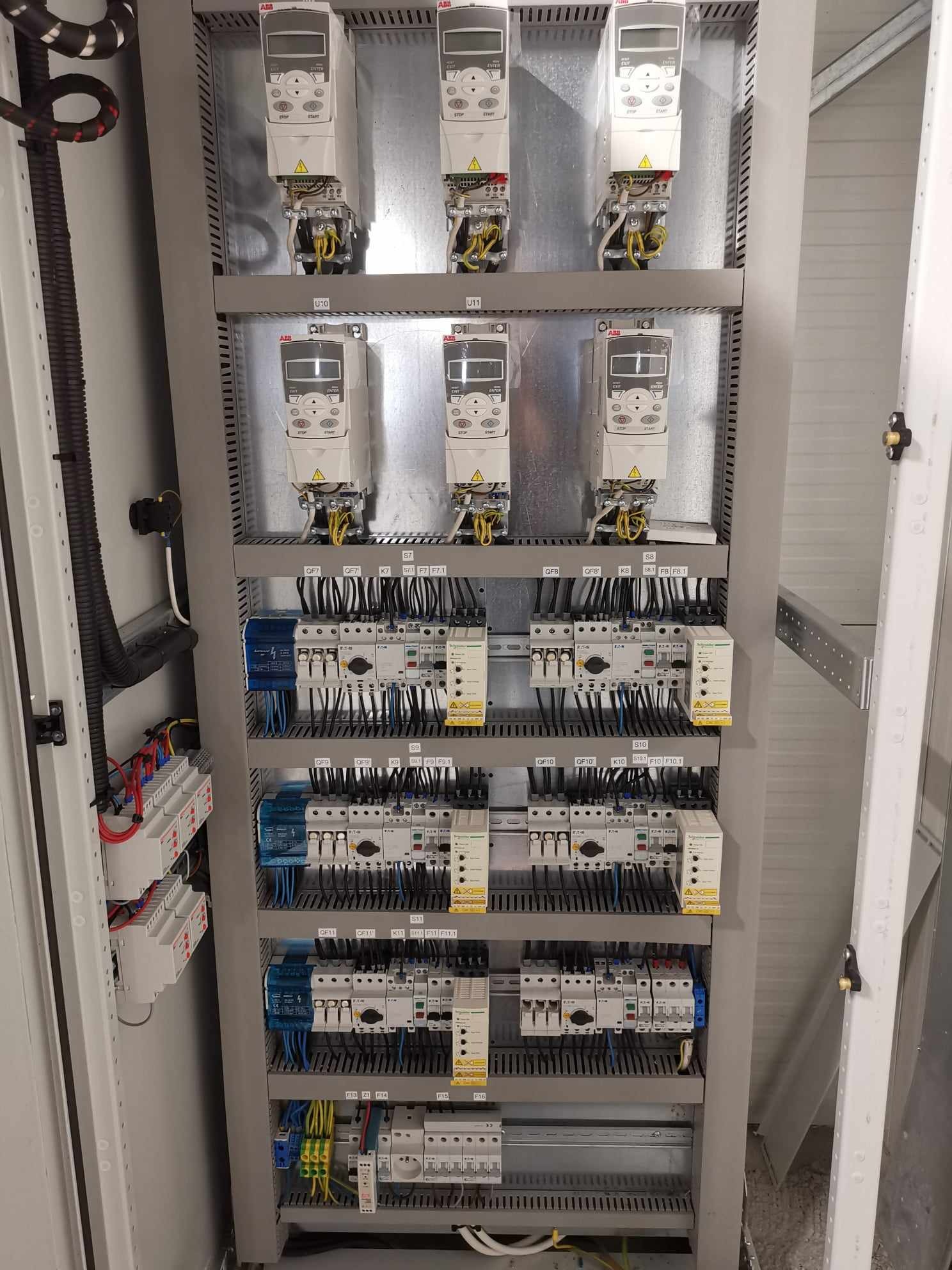 Wnętrze szafy sterowniczej z zamontowanymi falownikami ABB i modułami elektrycznymi, uporządkowane okablowanie, widoczne oznaczenia identyfikacyjne, szara obudowa szafy.
