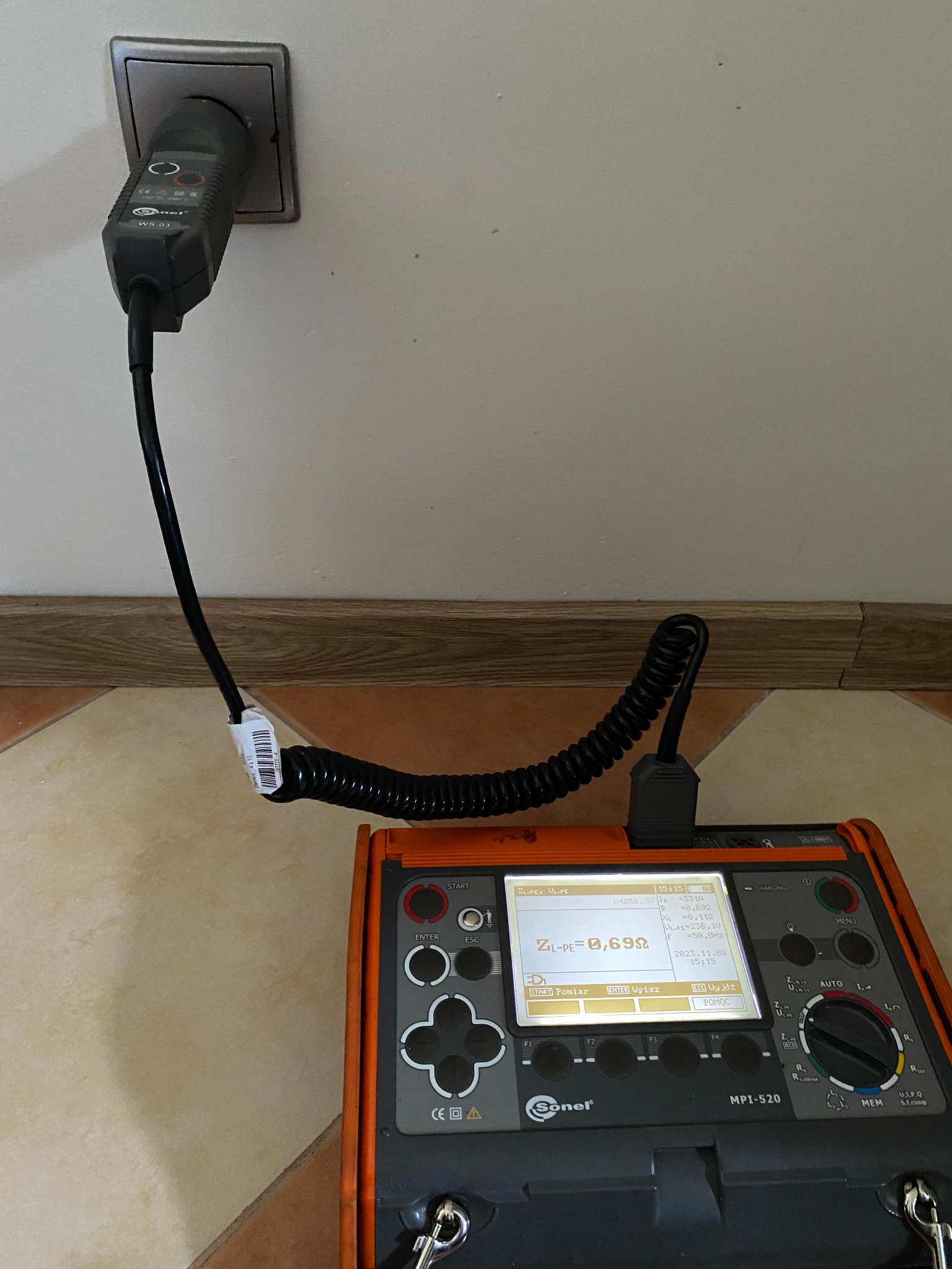 Miernik Sonel MPI-520 podłączony do gniazdka elektrycznego podczas pomiarów, wyświetlacz pokazuje wartość ZL-PE równą 0,69 Ω, widoczny kabel spiralny i wtyczka z etykietą