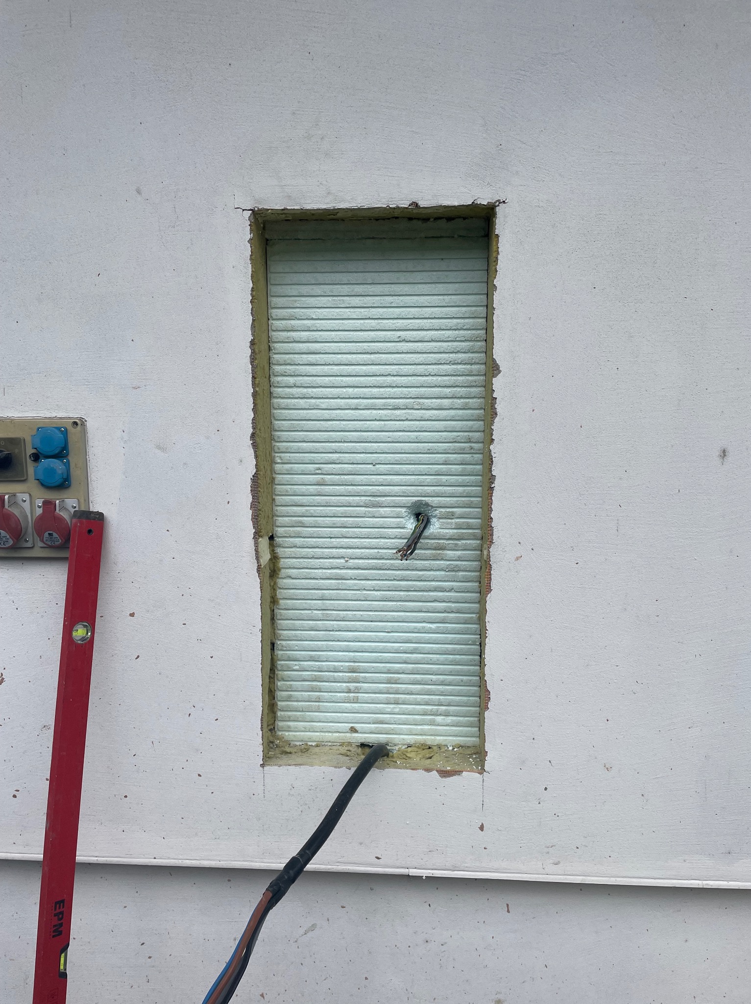 Przygotowanie otworu w ścianie w Domaradzu pod montaż rolety zewnętrznej, widoczne wystające przewody elektryczne i poziomica przy gniazdach.