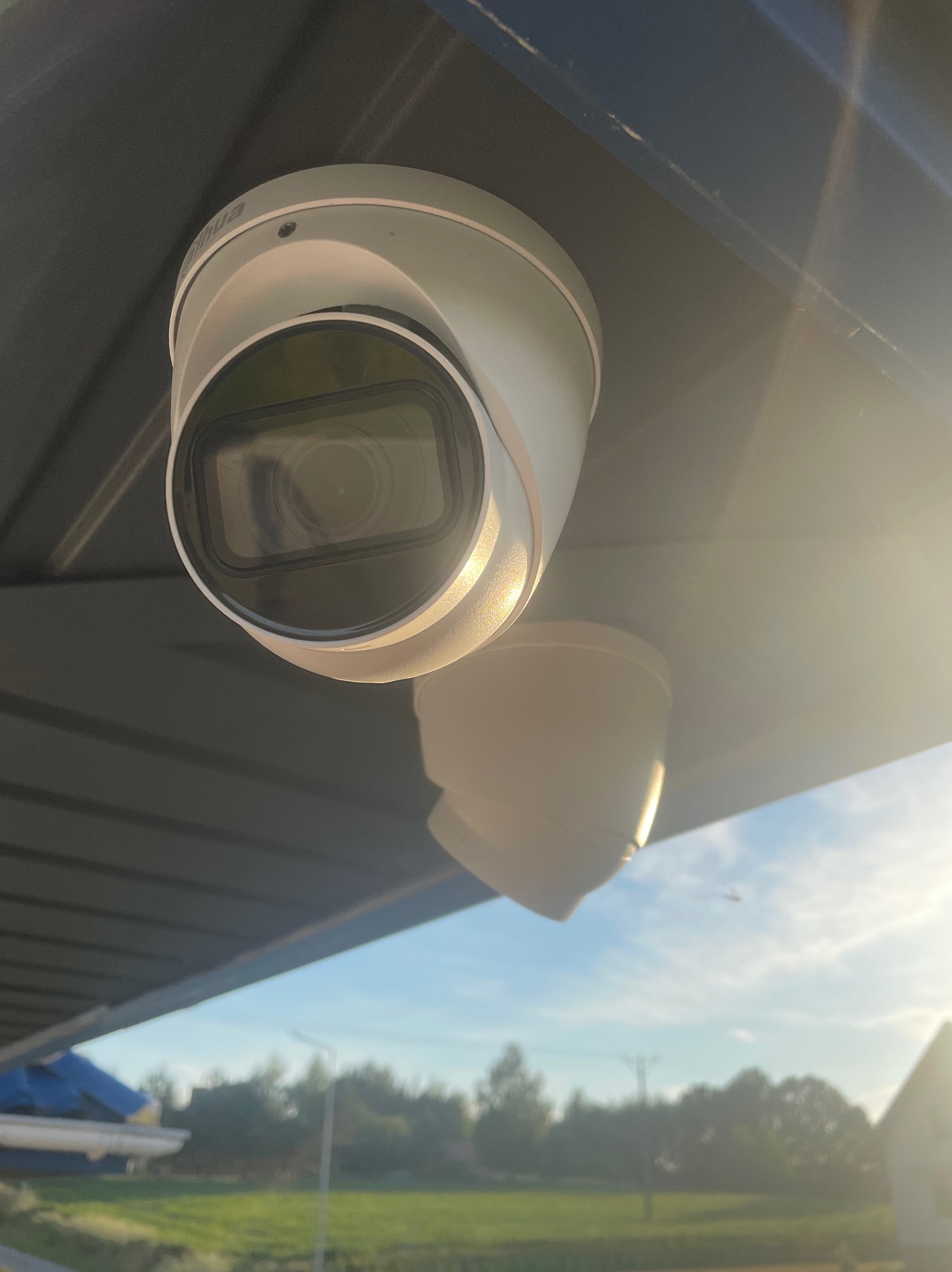 Dwie kamery monitoringu kopułkowe marki Dahua zamontowane pod zadaszeniem, widok na niebieskie niebo i zieleń w tle.