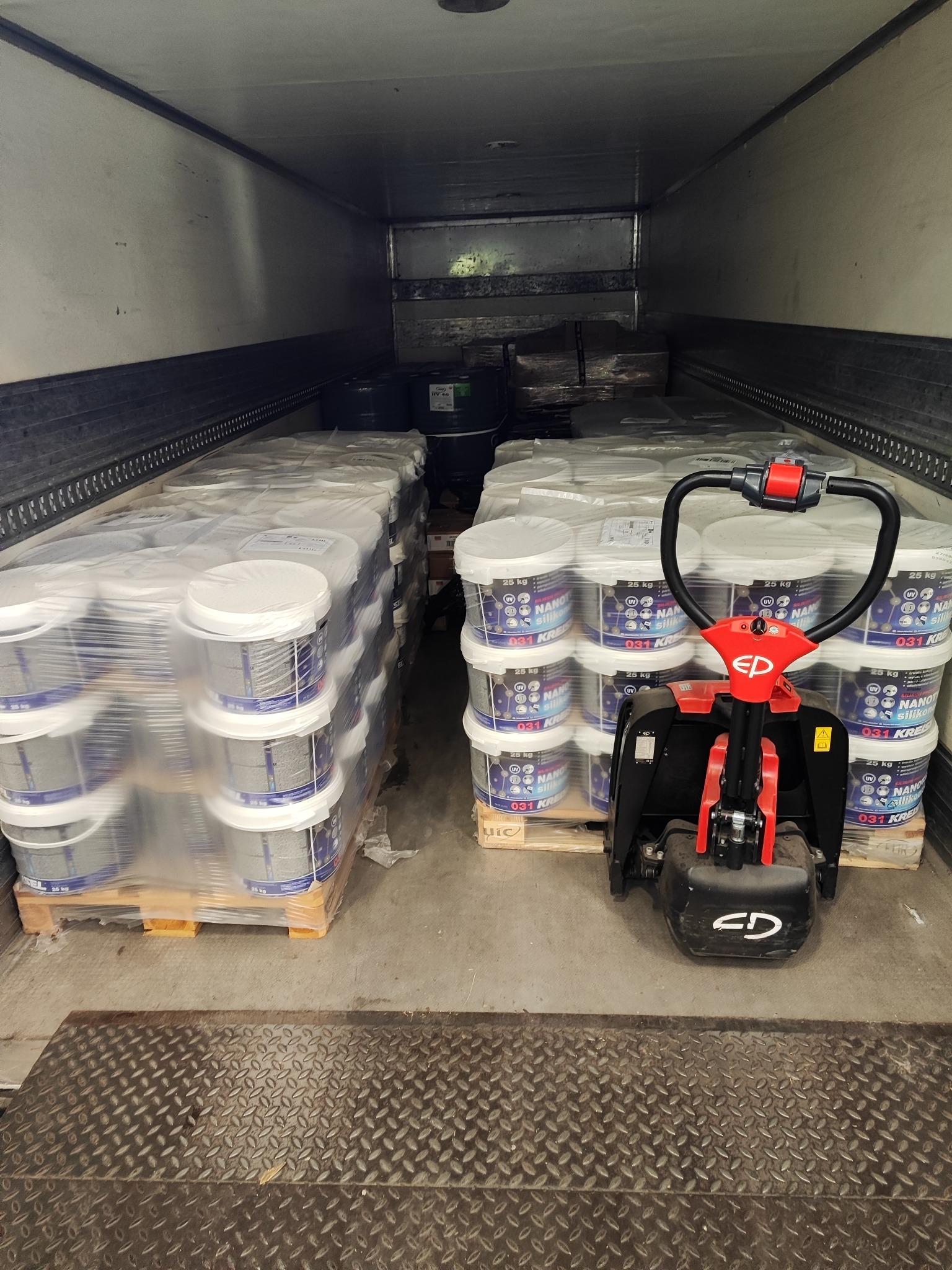 Wnętrze naczepy wypełnione paletami z wiadrami farby, widoczny wózek paletowy elektryczny z czerwonymi elementami. Wiadra owinięte folią stretch.