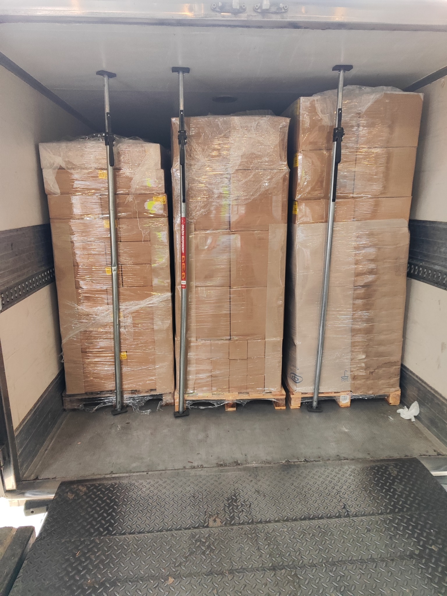 Wnętrze naczepy ciężarówki z trzema paletami kartonowych pudeł zabezpieczonych folią stretch i stalowymi rozpórkami.