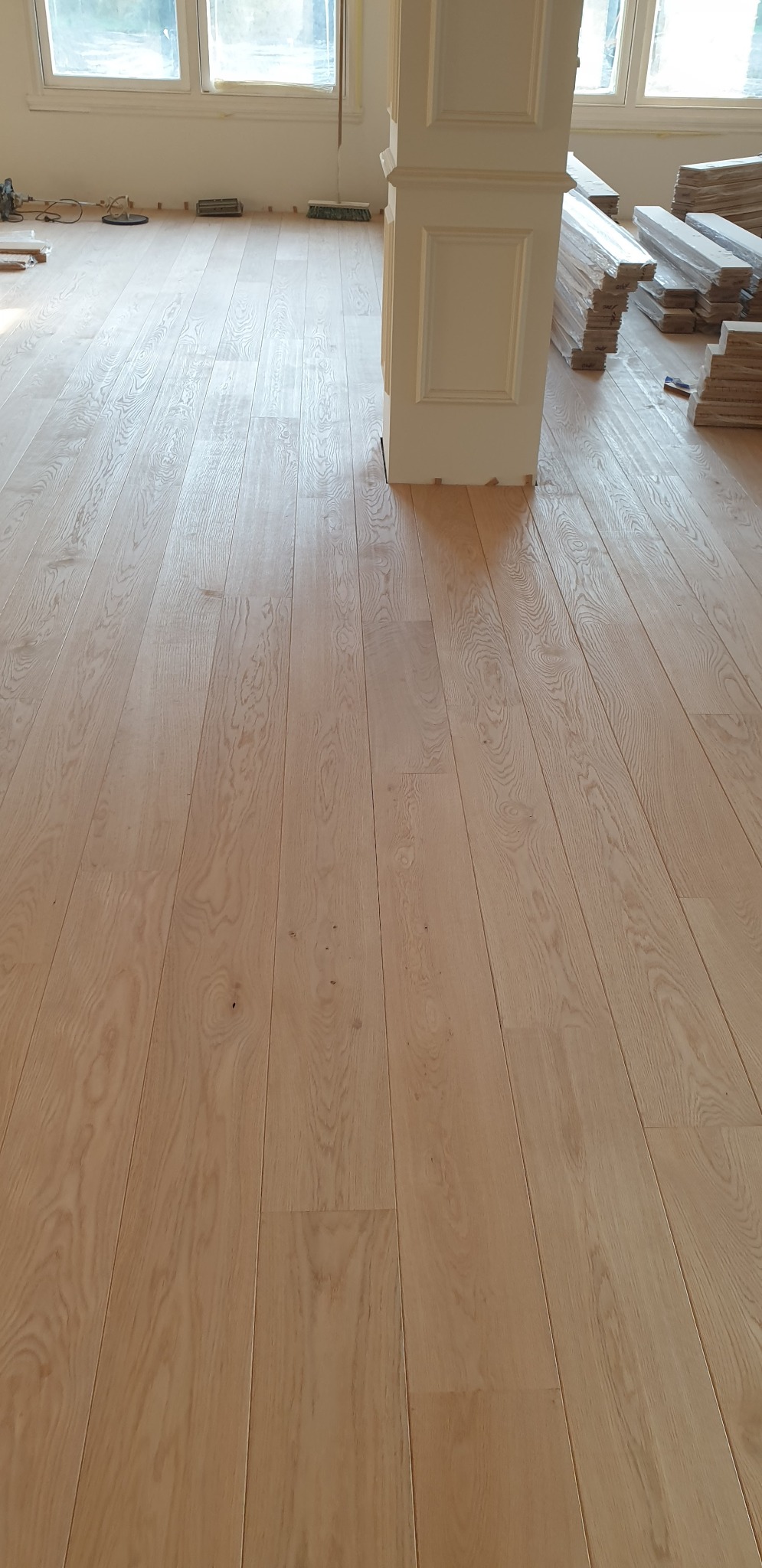 Jasny, świeżo ułożony parkiet z wyraźnym rysunkiem drewna w pomieszczeniu w Poznaniu, z kolumną dekoracyjną i paczkami desek w tle.