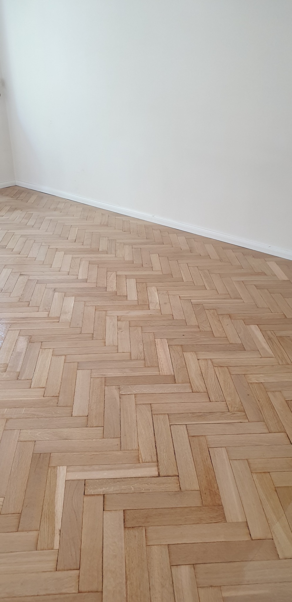 Ułożony parkiet w jodełkę, jasne drewno, widok z góry, białe ściany w tle.