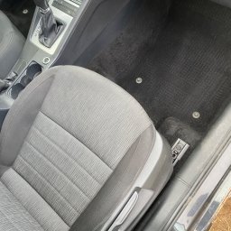 Brak - Wnętrze samochodu z czarnym dywanikiem i szarym siedzeniem kierowcy, widoczne ślady użytkowania na dywaniku.