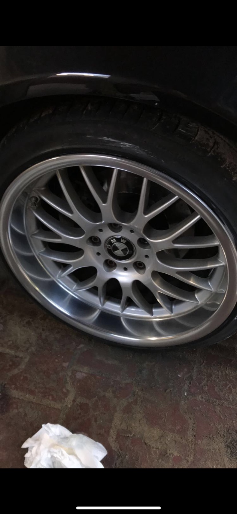 Aluminiowa felga BMW z oponą na tle brudnej, ceglanej nawierzchni i zmiętej chusteczki.