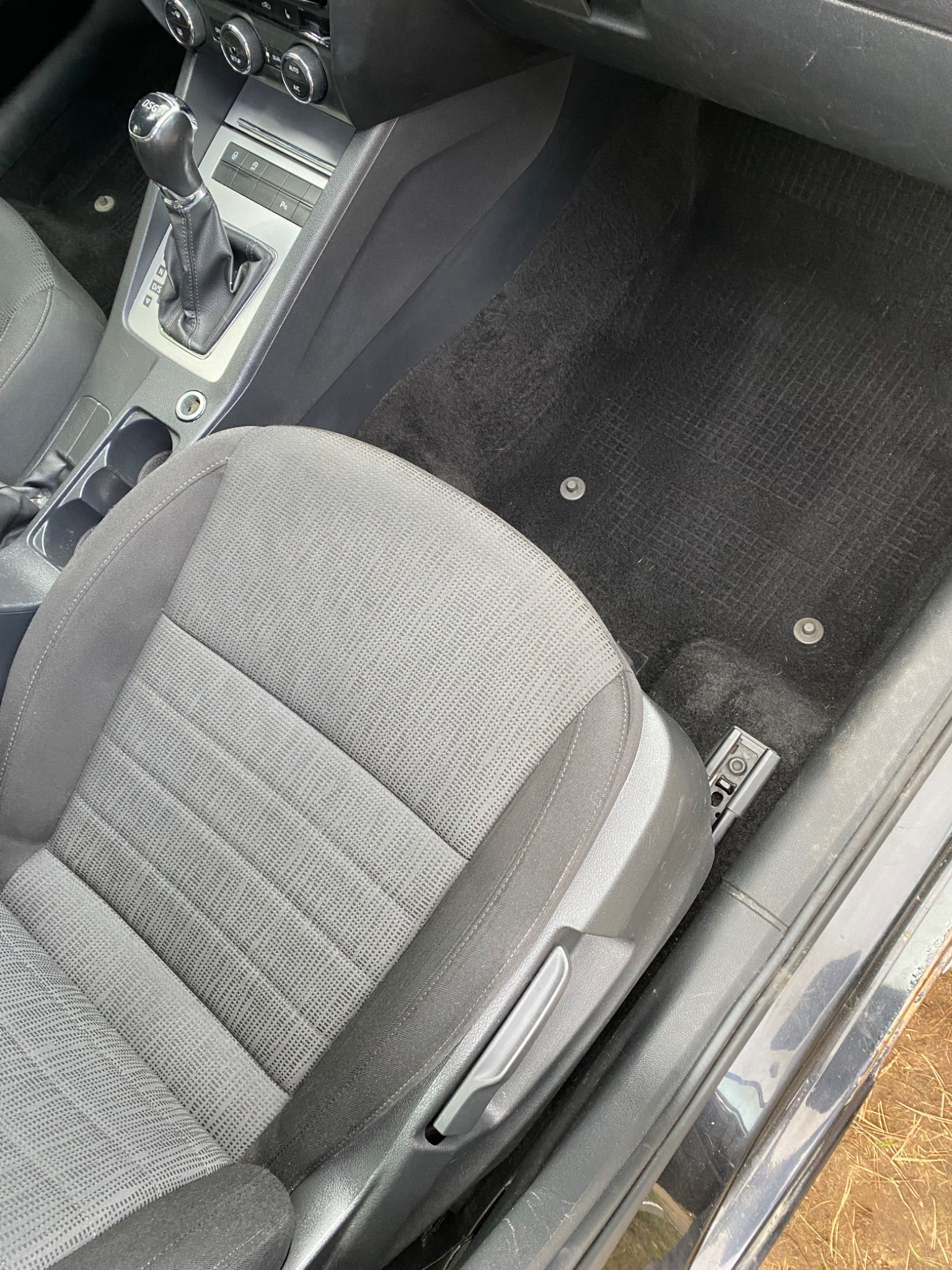 Wnętrze samochodu z czarnym dywanikiem i szarym siedzeniem kierowcy, widoczne ślady użytkowania na dywaniku.