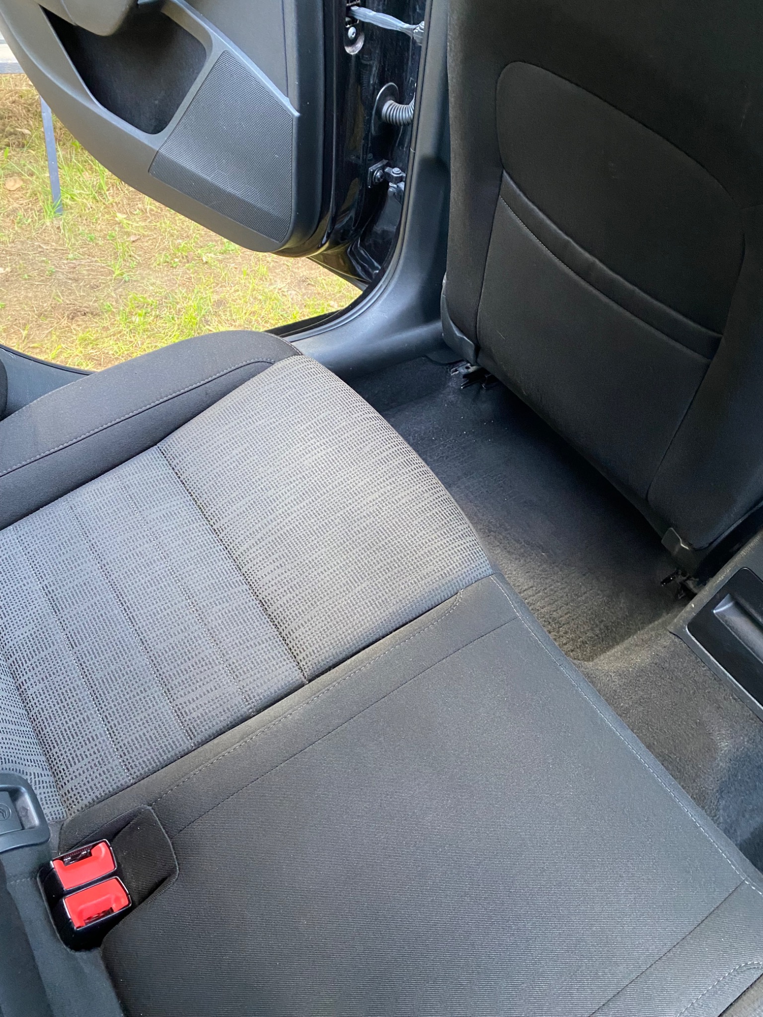 Wnętrze samochodu z widocznymi tylnymi siedzeniami i podłogą, ukazujące stan przed lub po czyszczeniu, otwarte drzwi.