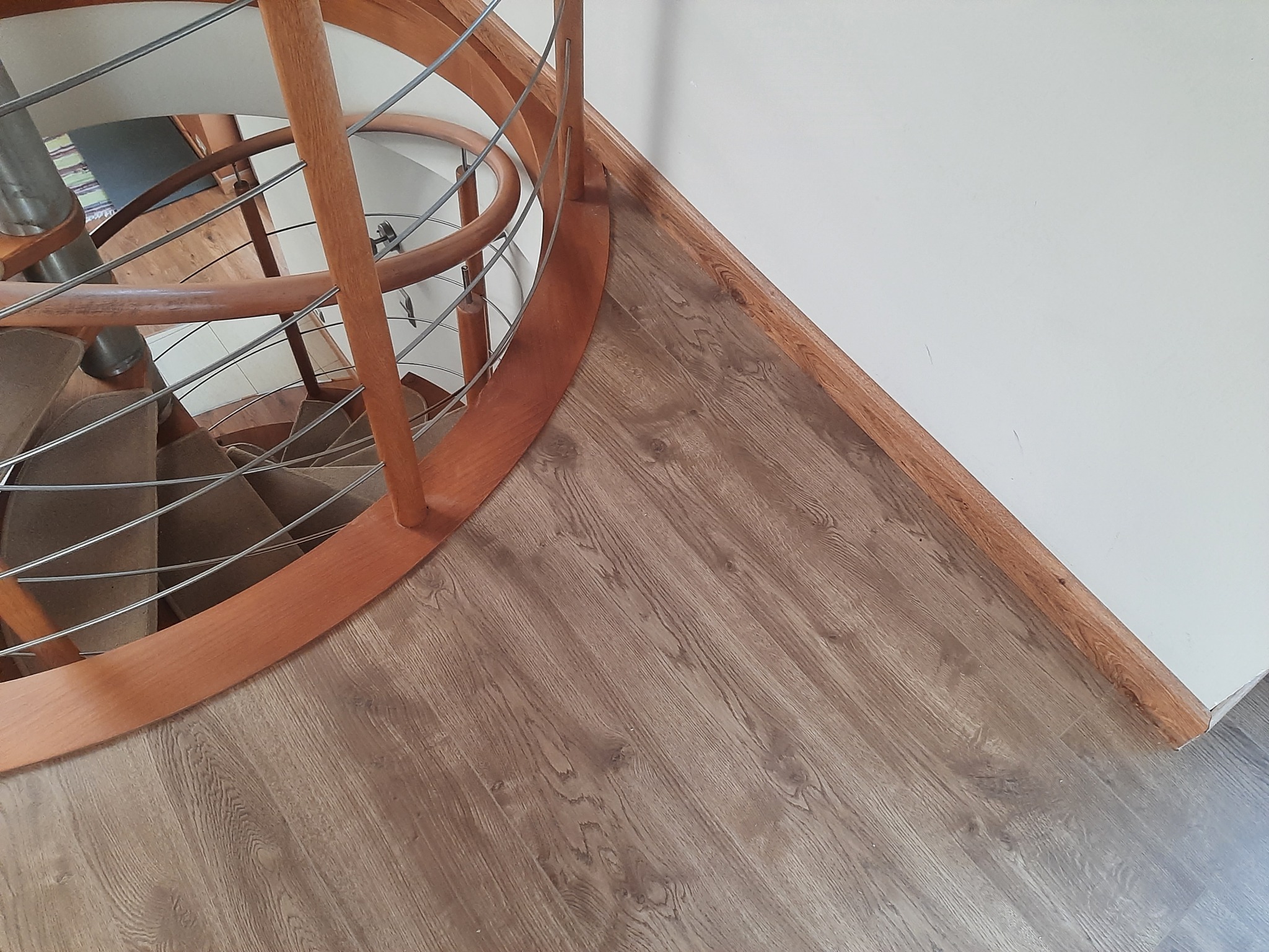 Fragment drewnianych, kręconych schodów z metalowymi poręczami na podłodze pokrytej panelami laminowanymi o wzorze drewna, widok z góry.