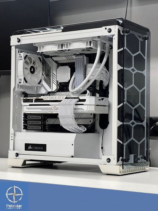 Wnętrze białej obudowy komputera stacjonarnego z przezroczystym panelem bocznym, ukazujące chłodzenie wodne, kartę graficzną GeForce RTX i zasilacz Corsair, całość utrzymana w estetyce bieli i srebra.