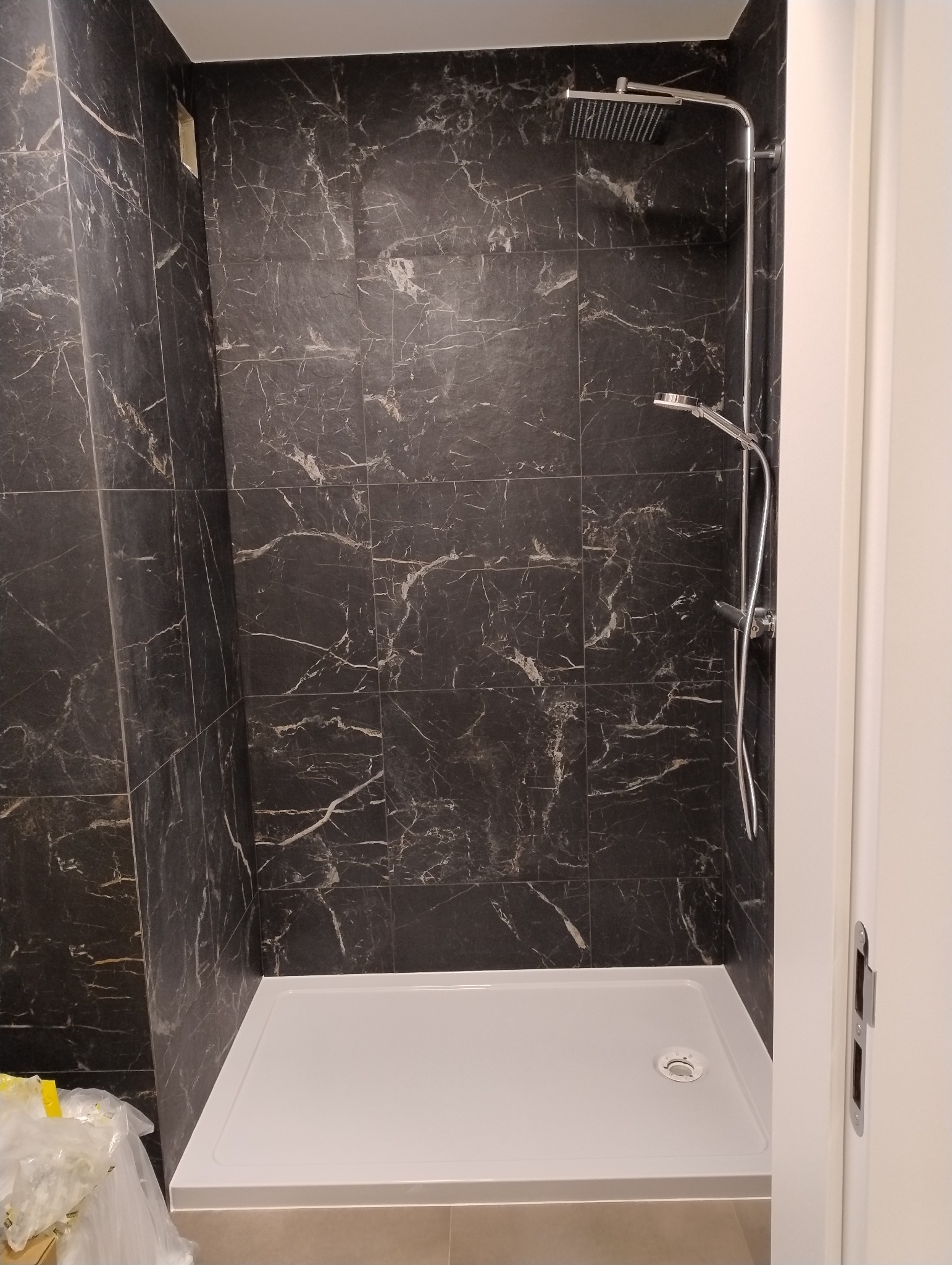 Kabina prysznicowa z czarnymi płytkami imitującymi marmur, biały brodzik i chromowana armatura.