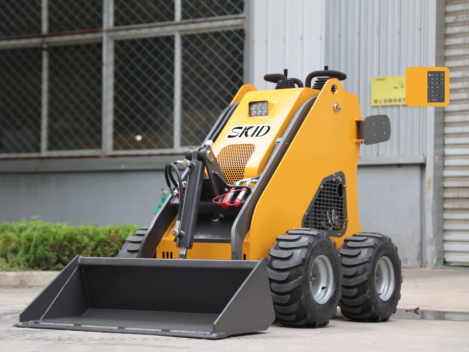 Żółta miniładowarka marki SKID, prezentowana w zbliżeniu na tle budynku z oknami zabezpieczonymi siatką, z widocznym panelem kontrolnym po prawej stronie.