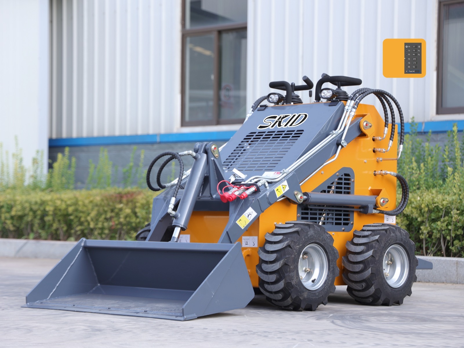 Pomarańczowo-szara miniładowarka LT-480W marki SKID stoi na betonowej powierzchni przed budynkiem przemysłowym i zielonymi krzewami.