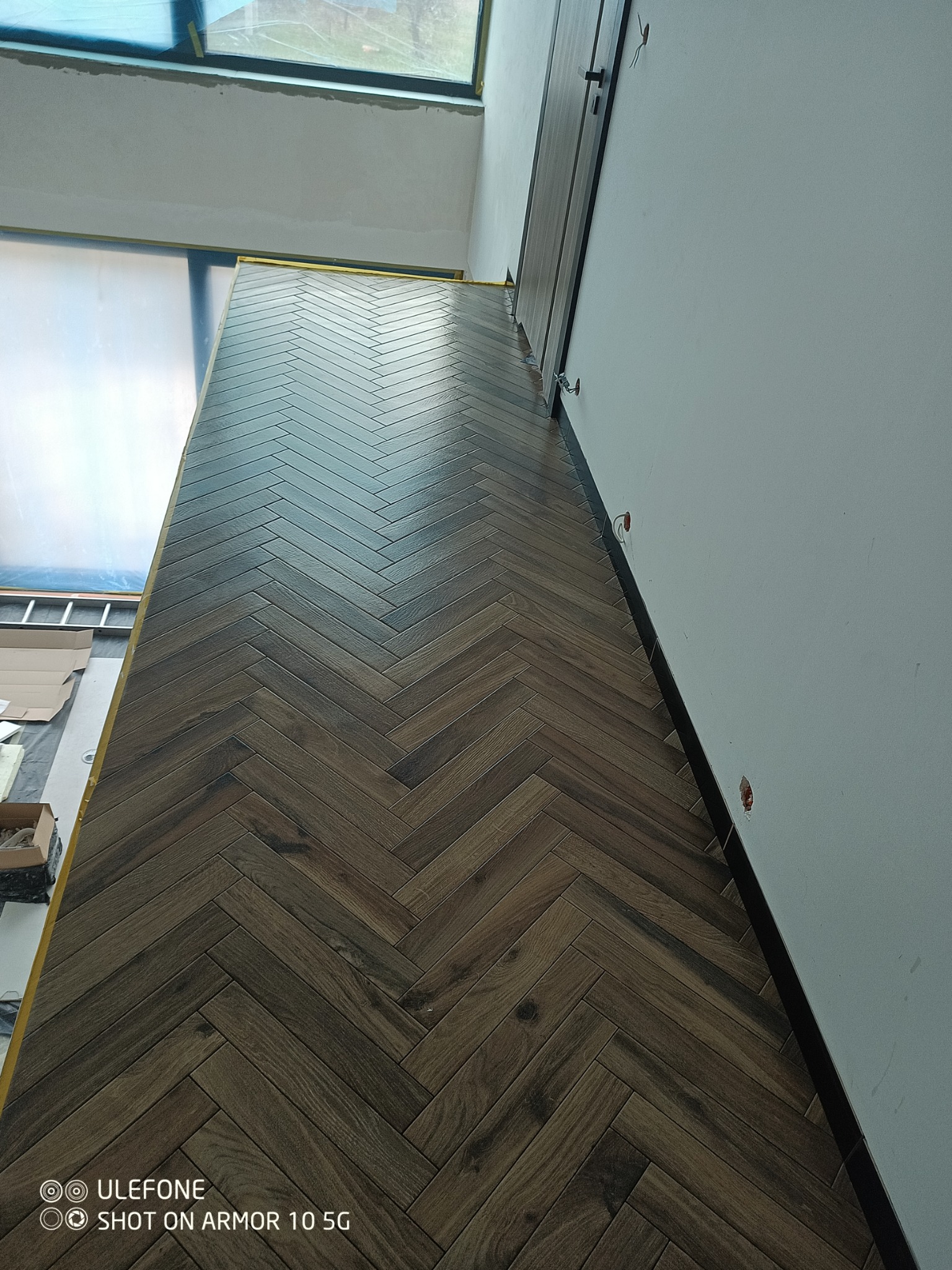 Ułożone panele podłogowe w jodełkę, widoczne niedokończone ściany i futryna drzwi, przygotowane do dalszych prac wykończeniowych.