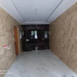 Wnętrze łazienki w trakcie wykańczania, widoczne marmurowe płytki na ścianach i podłodze, wystające kable elektryczne i surowa żarówka na suficie.