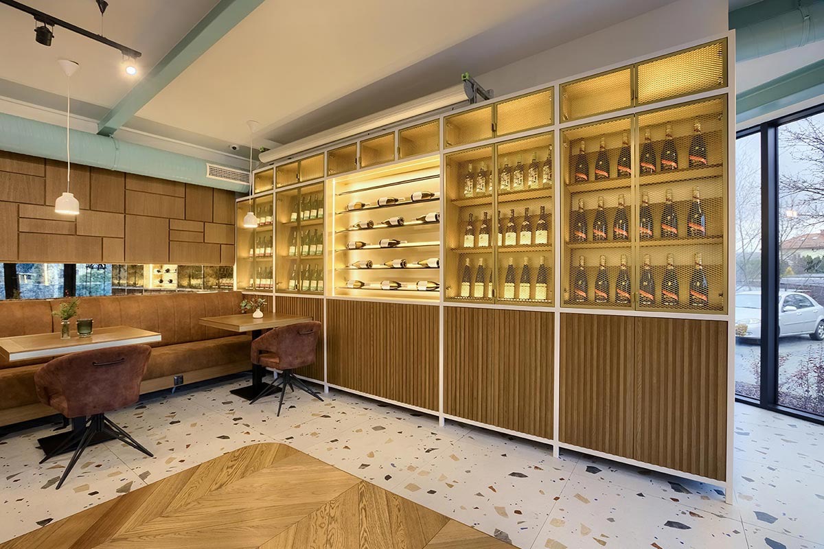 Wnętrze restauracji z regałem na wina podświetlonym LED, drewnianą boazerią i parkietem w jodełkę.