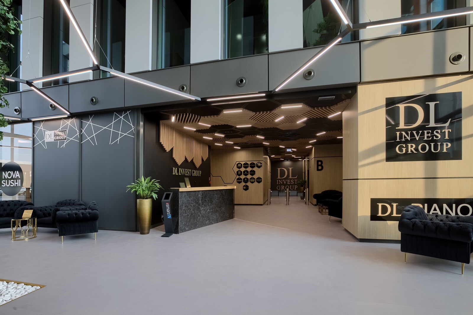 Nowoczesne wnętrze biura z recepcją, czarnymi sofami i dekoracyjnym oświetleniem sufitowym, widoczny napis DL Invest Group.