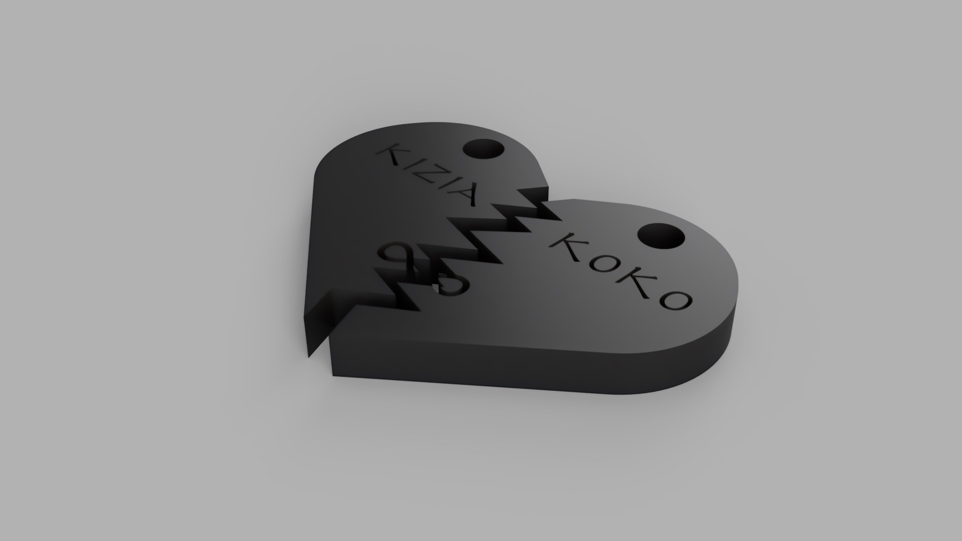Czarny, trójwymiarowy model złamanego serca z wygrawerowanymi imionami KIZIA i KOKO, widoczne otwory do zawieszenia.