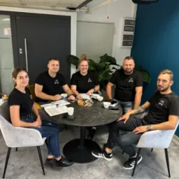 Zespół firmy z Tczewa siedzi przy stole w biurze, za nimi widoczna ekspozycja drzwi i okien.