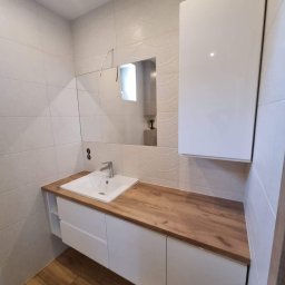 POWER-LAK - Nowoczesna łazienka w Kłocku z białymi szafkami pod umywalką z drewnianym blatem i wiszącą szafką nad umywalką, widok na lustro i wzorzyste płytki na ścianie.
