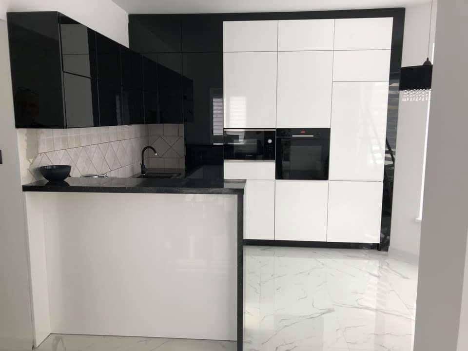 Nowoczesna kuchnia w czerni i bieli z błyszczącymi frontami, czarnym blatem i płytkami w romby nad zlewem, marmurowa podłoga.