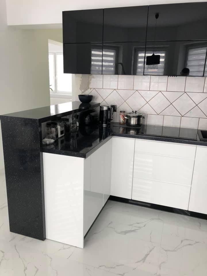 Nowoczesna kuchnia z czarnymi, błyszczącymi szafkami górnymi i białymi szafkami dolnymi, czarny blat z brokatem, białe płytki w romby na ścianie, marmurowa podłoga.