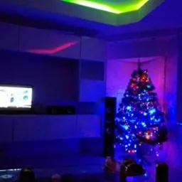 Pokój z sufitem podwieszanym z zielonym oświetleniem LED, choinką i meblami w odcieniach niebieskiego.