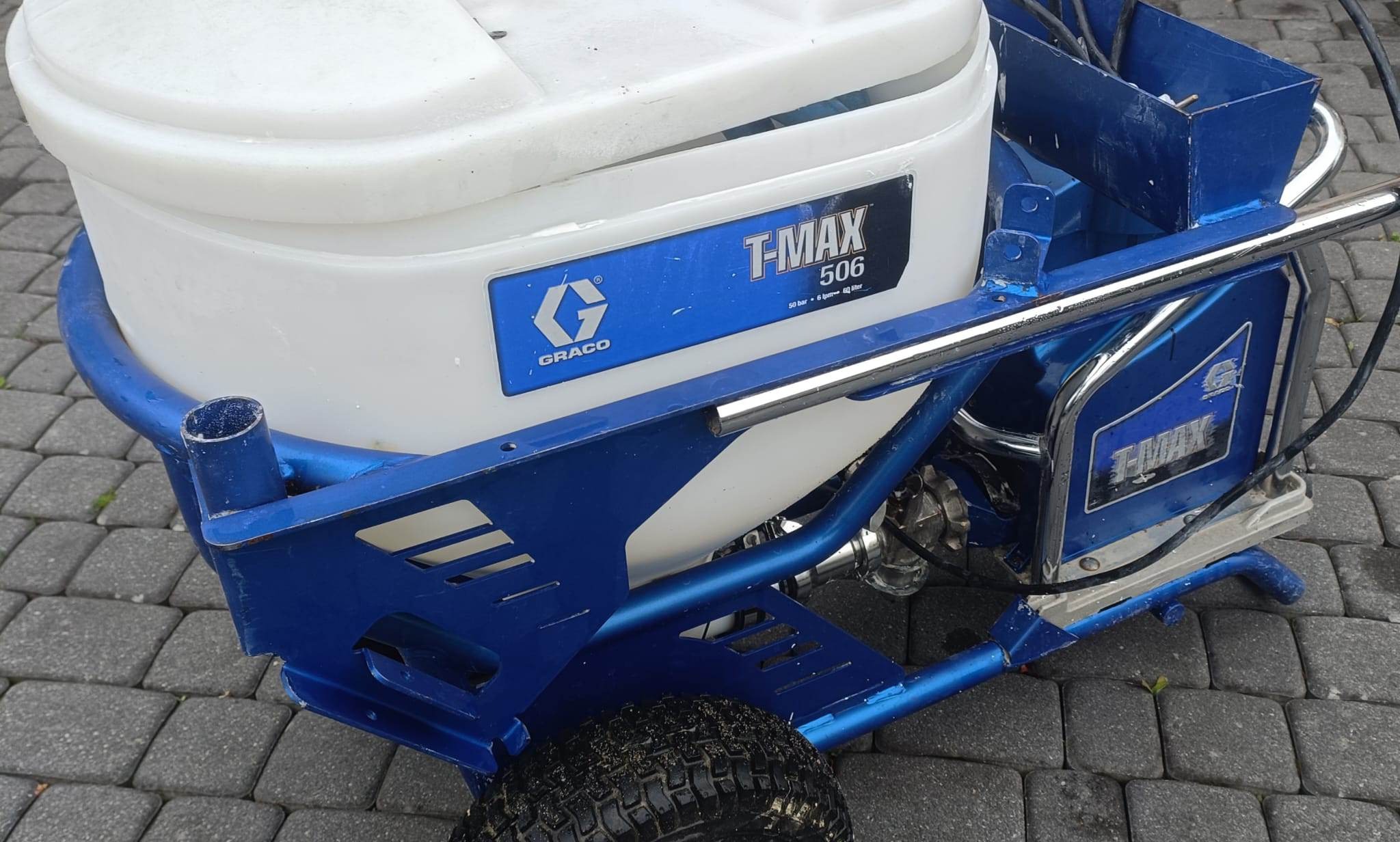 Agregat malarski Graco T-MAX 506 na kostce brukowej, widoczne detale konstrukcji w kolorze niebieskim.