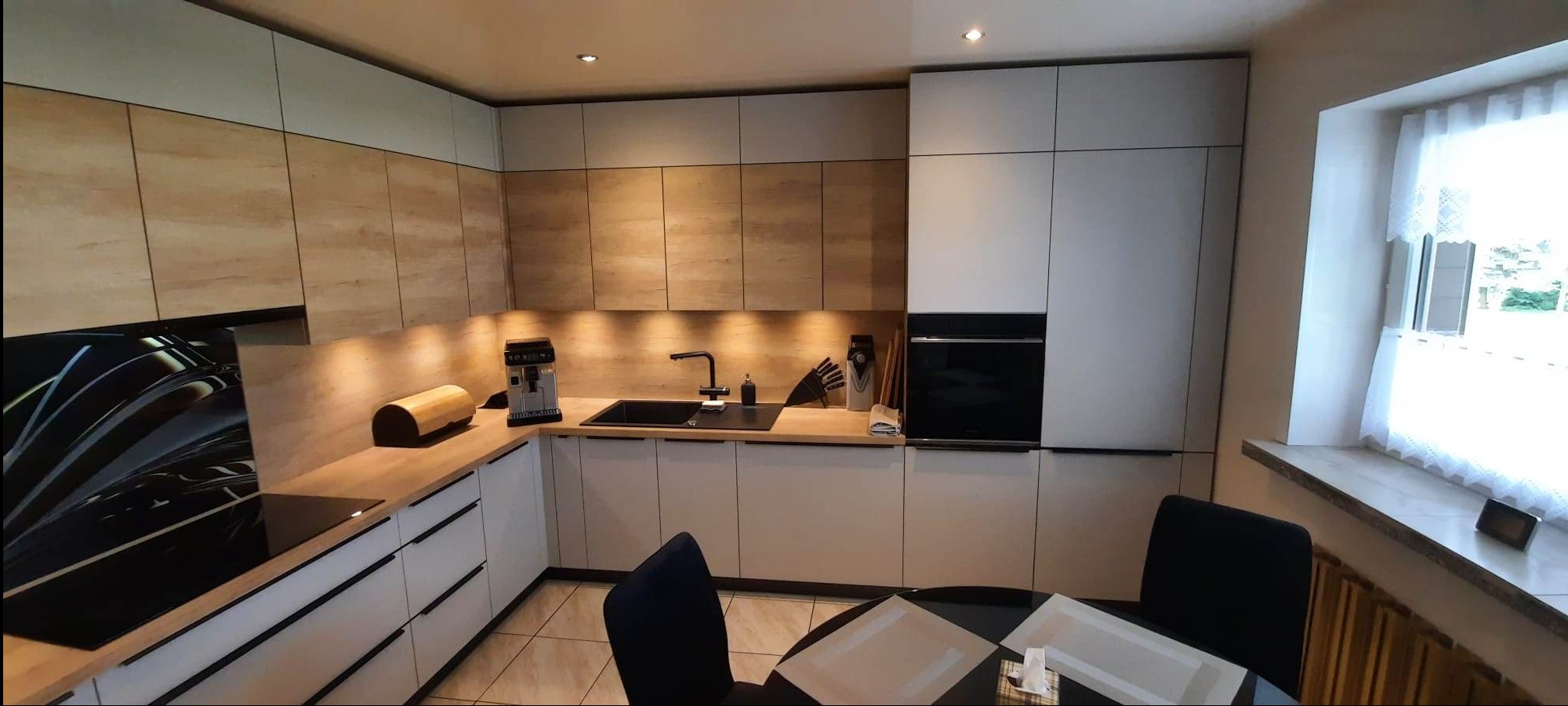 Nowoczesna kuchnia z frontami w kolorze kaszmiru i dębu Nebraska Naturalnego, czarne uchwyty Zobal UKW10, hartowana szyba ze wzorem na ścianie nad blatem roboczym, czarny zlew i bateria...