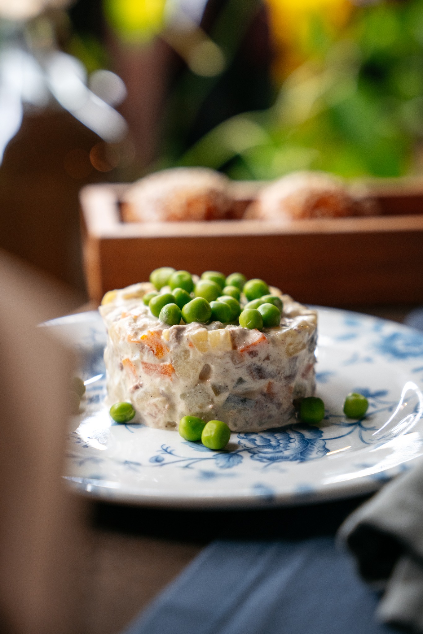 Warstwowa sałatka jarzynowa z groszkiem na wierzchu, podana na talerzu w stylu vintage z motywem niebieskich kwiatów.