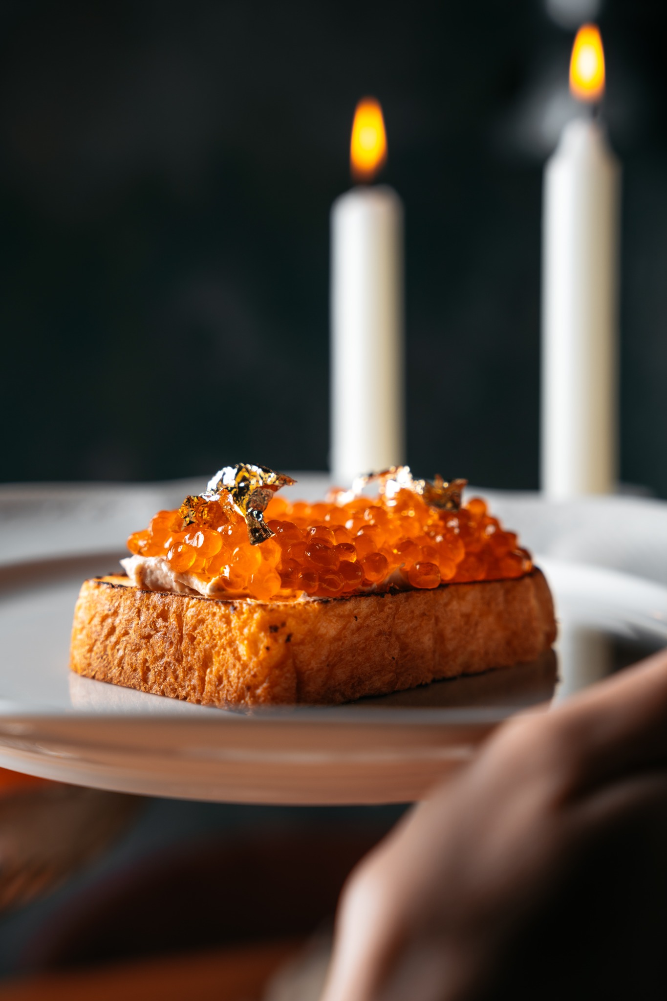 Kanapka z kawiorem i złotymi płatkami na talerzu, w tle dwie zapalone świece.