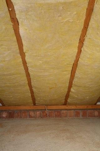 Żółta wełna mineralna między drewnianymi krokwiami poddasza, widok z dołu na izolację termiczną.