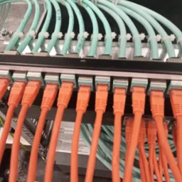 Panel krosowniczy z podłączonymi pomarańczowymi kablami Ethernet i niebieskimi kablami światłowodowymi, uporządkowanymi za pomocą opasek zaciskowych.