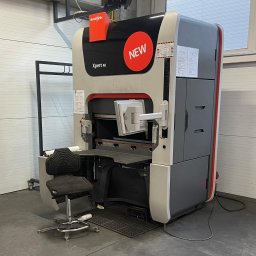 AD COMO GABRIELA SZEREMETA - Nowoczesna prasa krawędziowa Bystronic Xpert 40 z pomarańczowym logo i naklejką 'NEW', widoczna w hali produkcyjnej z szarą podłogą i białymi ścianami.