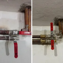 Miedziane rury instalacji wodnej z zaworami kulowymi o czerwonych uchwytach, zamontowane przy suficie z widocznymi śladami po kuciu.