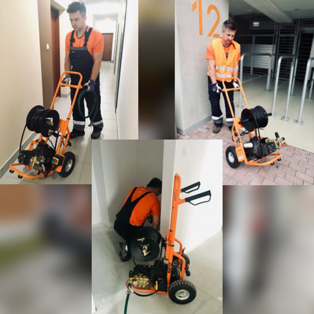 Hydraulik w pomarańczowej koszulce i czarnym kombinezonie obsługuje pomarańczowe urządzenie do czyszczenia kanalizacji wewnątrz budynku.