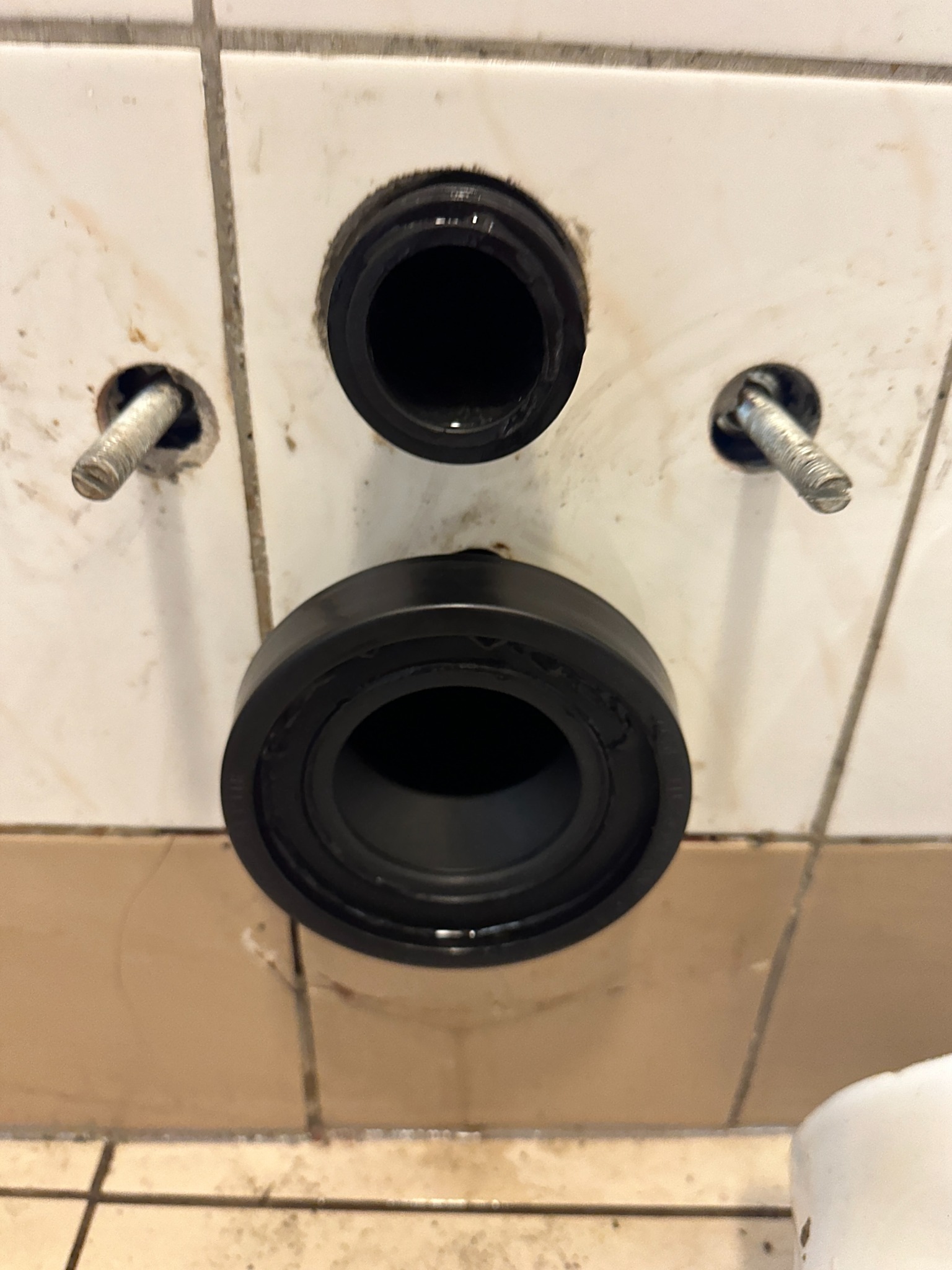 Przygotowane otwory w glazurze i zamontowane uszczelki do podłączenia toalety, widoczne śruby mocujące.