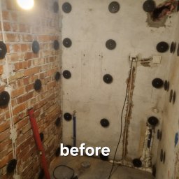 WOJCIECH BIESIADA - Zdjęcie przedstawia fragment łazienki w trakcie remontu, widoczne stare płytki częściowo usunięte, odsłonięta cegła, ściany z widocznymi otworami i zamocowanymi elementami mocującymi, instalacje...