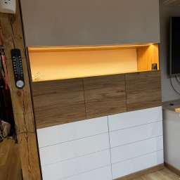 WOJCIECH BIESIADA - Biało-drewniana szafa z oświetleniem LED, wbudowana w nierówną ścianę z drewnianą belką i termometrem na niej.