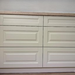 WOJCIECH BIESIADA - Fronty szuflad w zabudowie kuchennej, kremowe, z frezowanymi ramkami, drewniany blat, widok z bliska.