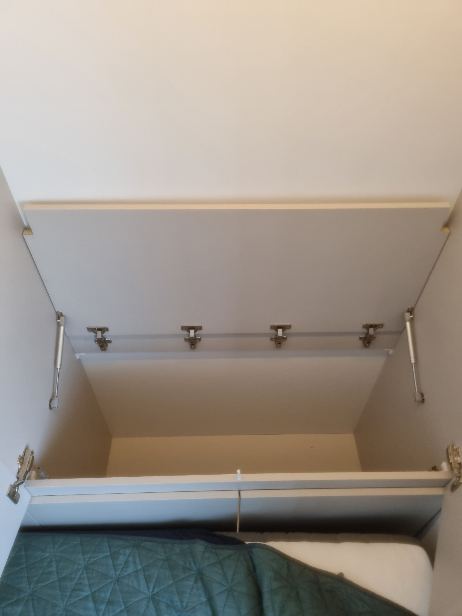 Wnętrze szafy z otwartymi drzwiami na zawiasach gazowych, widoczna półka z tekstyliami w odcieniach zieleni i bieli.