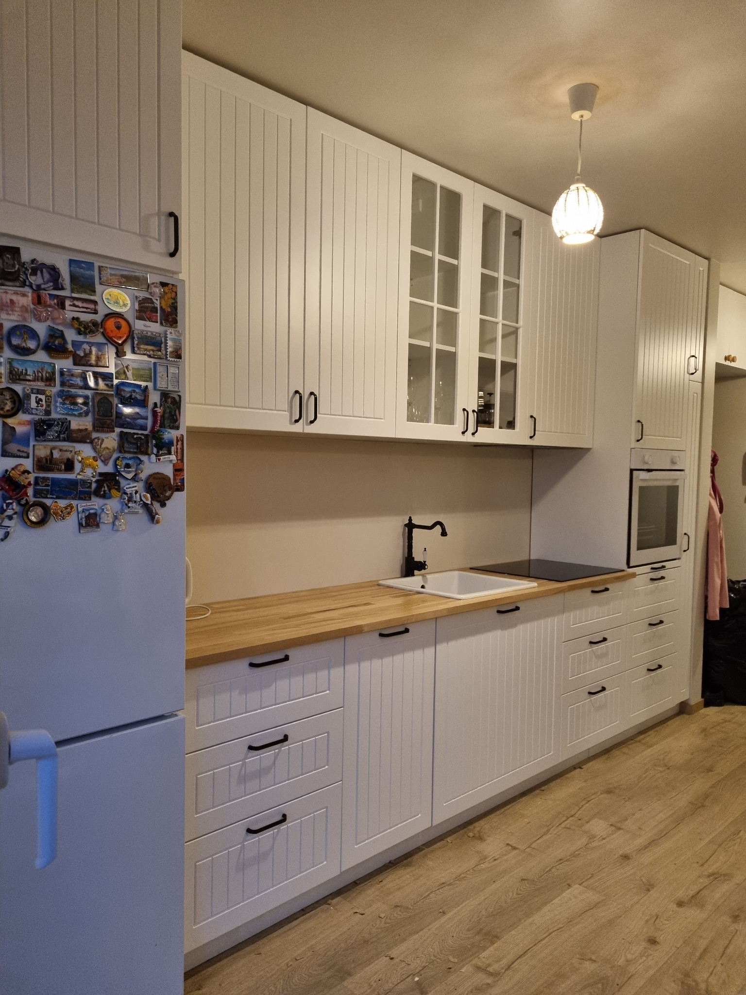 Biała kuchnia z drewnianym blatem, czarną armaturą i magnesami na lodówce.